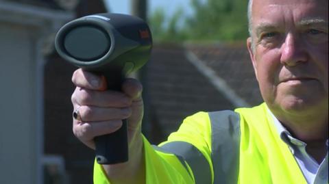 A volunteer holding a speed gun by the side of a road in South Kyme
