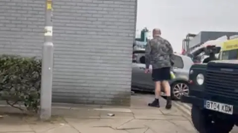 Dylan Winborne A man is standing near to where the car has crashed through the wall, with emergency services nearby.