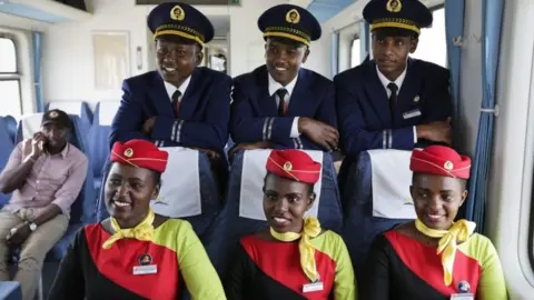 EPA Kenya Railways train attendants (R) pose for a photograph inside one of the new passenger trains using the new Mombasa to Nairobi Standard Gauge Railway (SGR), constructed by the China Road and Bridge Corporation (CRBC) and financed by Chinese government, during a test run of the train in Mombasa, Kenya, 29 May 2017