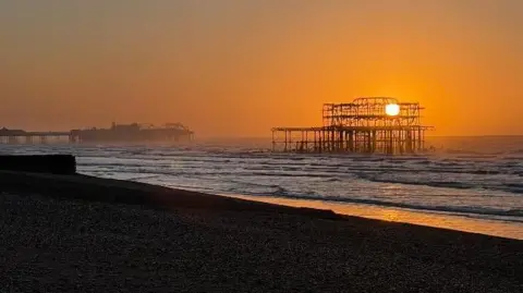 BeachStrollerRoly A burnt-out Victorian pier. It is out at sea and the sun is rising. 