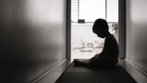 kieferpix/Getty Images Young child sitting in a hallway with their head bowed