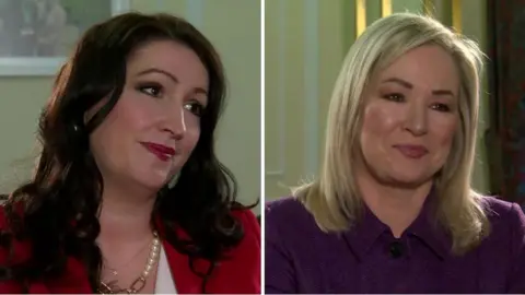 BBC Emma Little-Pengelly and Michelle O'Neill being interviewed by BBC News NI.  Emma has long, dark curly hair and is wearing a red jacket and a white blouse.   Michelle has shoulder-length straight blonde hair and is wearing a purple tweed suit. 