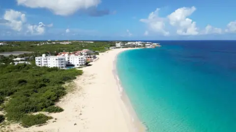 BBC/Andy Alcroft Drone shot of Anguilla, showing a bright blue sea to the right and golden sand to the left