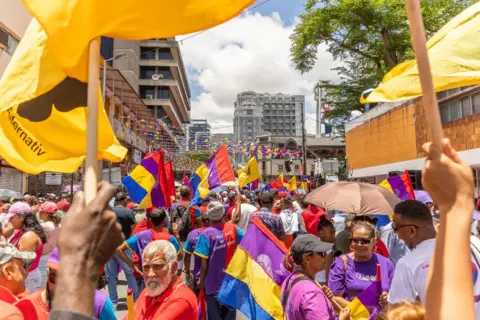 Laura Morosol / AFP Change Alliance supporters in mainly red, purple T-shirt hold flags as they gather to attend a campaign rally - bunting in the party colours - purple, yellow, red and blue - can also be seen in Port Louis, Mauritius - Sunday 3 November 2024