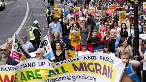 Reuters Protesters carry a sign that says "we are all migrants" on a city street 