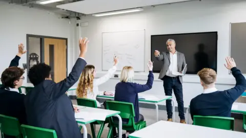 A classroom full of school children in a lesson with a teacher at the front of the class
