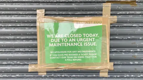 A green sign with white text is taped to a grey door. The tape is brown.
