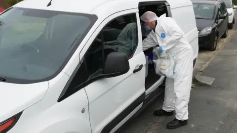 A person in a hazmat suit looking in a car