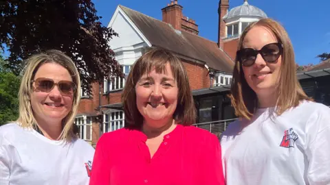 Victoria Stonehouse and Emma Perkins wearing white t-shirts with 'Stand Against MND' branding, standing next to Nottinghamshire Hospice boss Rachel Hucknall who is wearing a bright pink top.