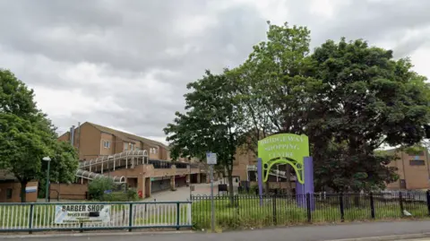 A red brick shopping centre with a green and purple sign in front