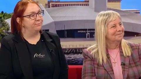 On the set of BBC Breakfast Charlotte Hennessy (L) has long red hair. dark glasses and is wearing a dark jacket and top while Margaret Aspinall (R) has long grey/blonde hair a tartan jacket with shades of brown and violet and a pink top. She wears a gold cross on a chain.