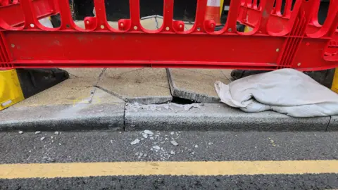A close-up image of a damaged pavement surrounded by red barriers.