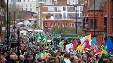 A sea of people waving colourful flags, including Irish ones, throng a street in Birmingham.