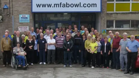Peter Jordan A group of about 100 people standing together outside a bowling alley.