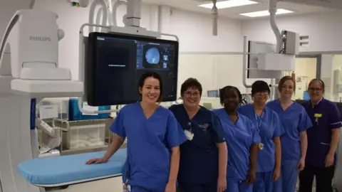 NWAFT Six hospital staff wearing blue scrubs stand in front of a blue procedure bed, which is next to the new equipment.