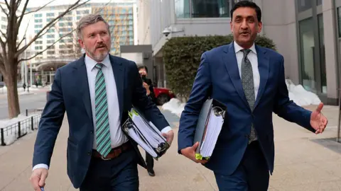 Getty Images Lawmakers Thomas Massie and Ro Khanna walking side-by-side on a street, wearing suits, and carrying large binders of files