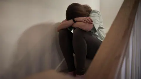 A woman sits on a staircase with her head resting on her crossed arms.