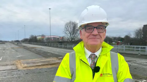 Gateshead Council leader Martin Gannon wears a white hard hat and yellow hi-vis coat while standing on the deserted flyover in Gateshead.