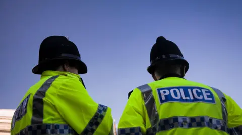 Two police officers wearing black helmets and hi-vis coats with their backs to the camera