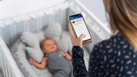 Woman using a phone in front of a baby in a cot