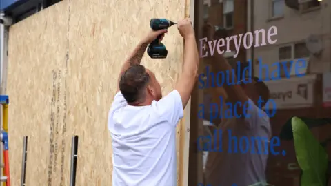 Reuters A man in a white t-shirt screws boards to the front of the shop to prevent damage from rioting