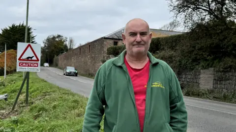 Dave Webb, founder of the UK Wild Otter Trust standing by an otter warning sign