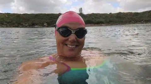 A swimmer in a pink swim hat and wearing goggles in the sea.