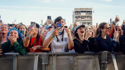 Ceremonia de victoria/Isla fuerte Louis Tomlinson frente a una multitud de fanáticos en las barricadas. Se ven muy emocionados y la mayoría están filmando en sus teléfonos. En el centro hay una mujer con una camiseta de Inglaterra.