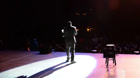Getty Images A man standing on stage with a crowd in front of him