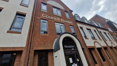 The exterior of Solihull Council's headquarters. It is a red and white brick building with lots of windows. The words "Council House" are emblazoned on the front. A door under a small archway is labelled "Reception".