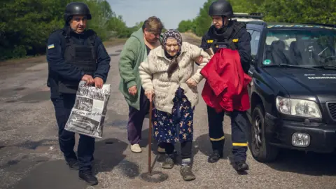 An elderly Sumy region resident is evacuated from her village with the help of two men