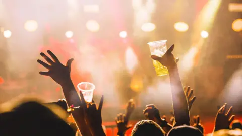 Crowd at a concert. Hands are holding up plastic cups.