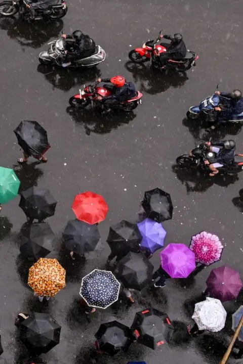 Dibyangshu Sarkar/Getty Images Commuters wait with umbrellas for transport in Kolkata, India
