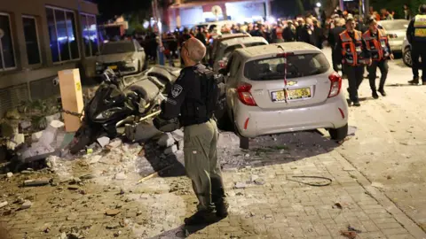 A first responder gazes upwards at the site of a cluster bomb strike. 