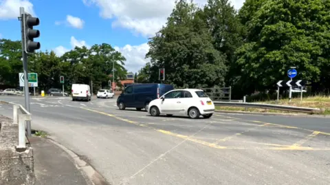 Cars driving around a round-about with three lanes and arrows pointing.