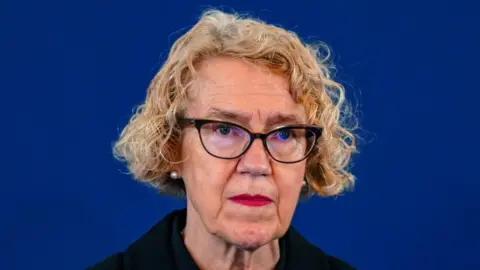 PA Media Public inquiry chair Lady Justice Thirlwall. She has curly blonde hair and wears black oval glasses. She appears in front of a dark blue backdrop.