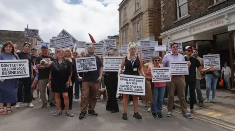 A few dozen protesters are holding placards which say parking charges will be the death of the high street