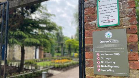 A picture of the gate to Queen's Park, Swindon. The sign on the gate clearly says "no dogs". 
