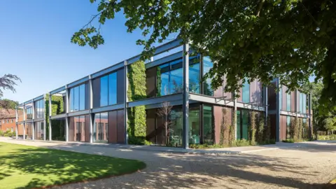 WilkinsonEyre A modern industrial-looking two-storey building, which has a mixture of large windows, copper cladding and protruding steal beams on its exterior.