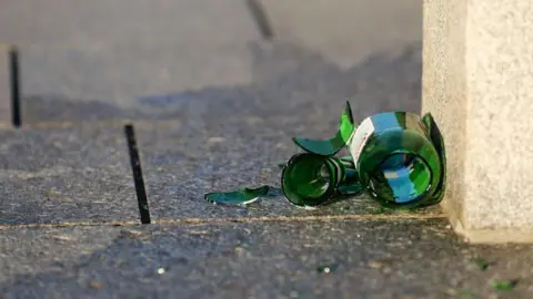 Stock image of a broken green beer bottle lying on a pavement.