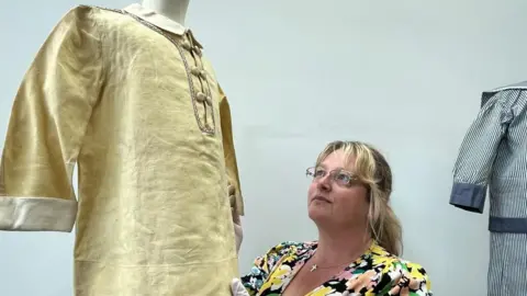 Leeds City Council A woman wearing glasses and a floral dress examines a gold-coloured shirt