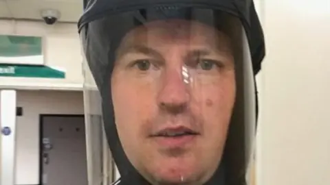 A man in a protective mask looks at the camera