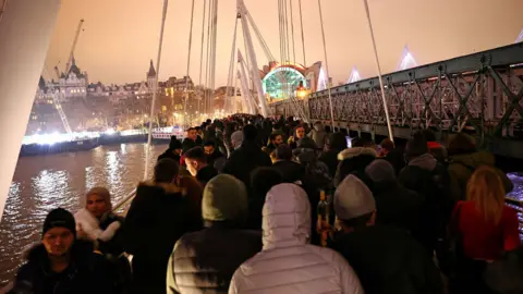 Reuters People walk along Hungerford Bridge during an anti-lockdown demonstration and a New Year"s celebration, amid the outbreak of the coronavirus disease (COVID-19), in London, Britain January 1