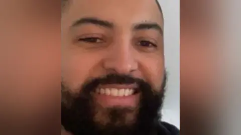 West Midlands Police A close-up photo of a man with a black beard and close-cut black hair.