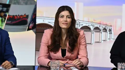 Laila Cunningham appears on Sunday with Laura Kuenssberg as a panelist. She wears a pink jacket and looks at the camera from behind a desk 