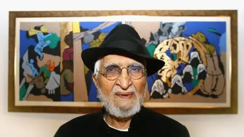 Indian artist MF Husain wearing a black jacket with white shirt and a black hat poses in front of one of his paintings in Raan bar at the O2 Arena on July 3, 2007 in London