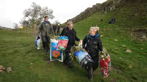 PA Media National Trust rangers carrying plastic bags filled with small branches from the chopped down sycamore