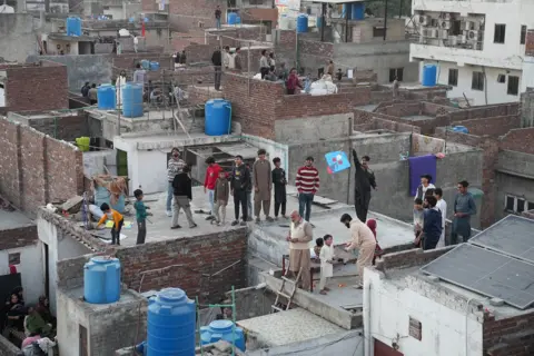 Sh Ed Kamil Khan People on rooftops look up to the sky 