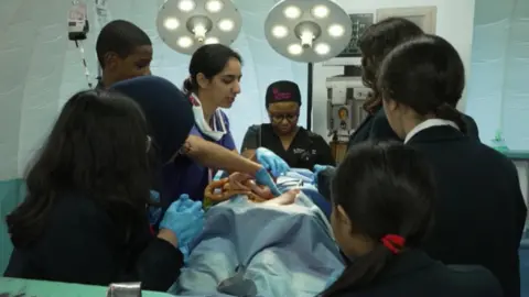 Students are shown a simulated scene of an operating theatre