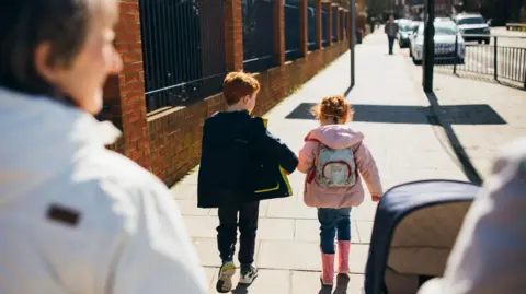 Getty Images A family walk along a footpath with parent pushing a pram and grandparent alongside. The two children are dressed in jackets and denim jeans.